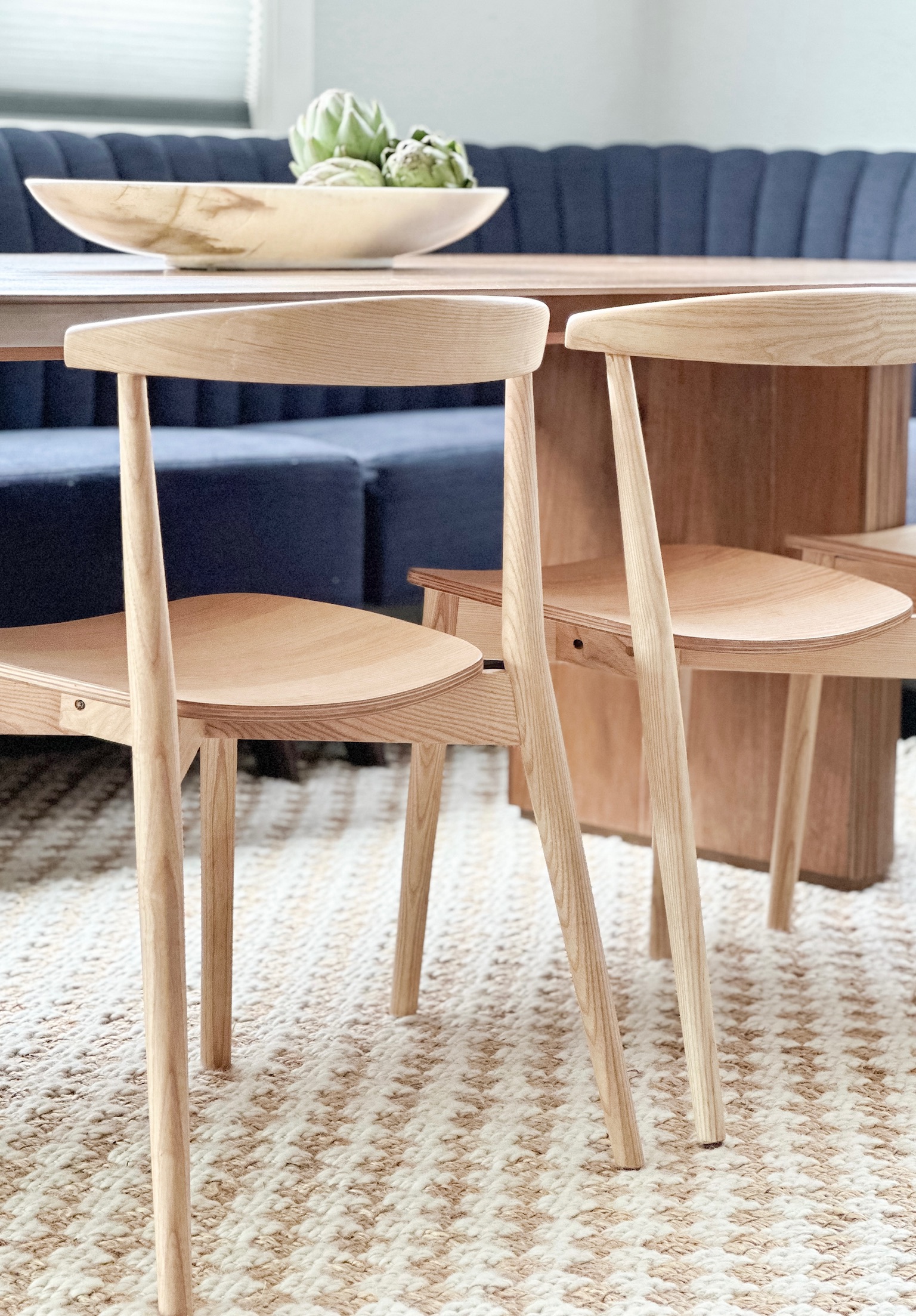 Back of natural wood chairs on a woven checkered rug with a blue banquette.